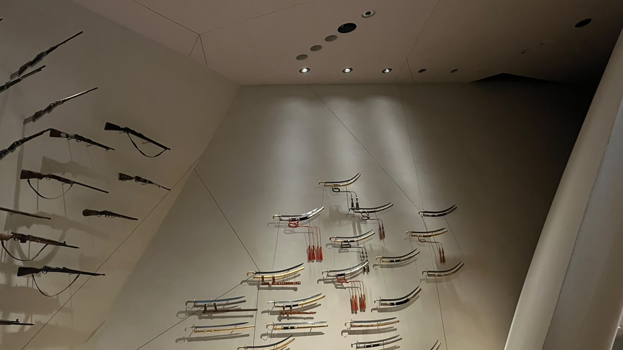 Curved swords illuminated on a museum wall, casting distinct shadows behind them.