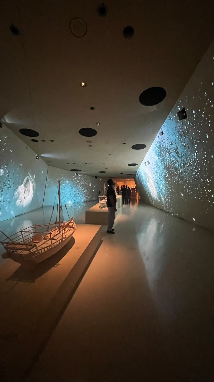 A warmly lit wooden boat model surrounded by blue wall projections.