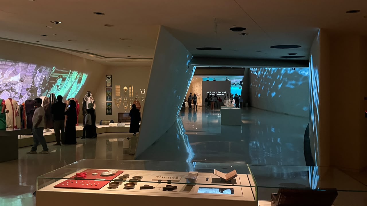 An illuminated display case in front of gallery walls covered with projected imagery.